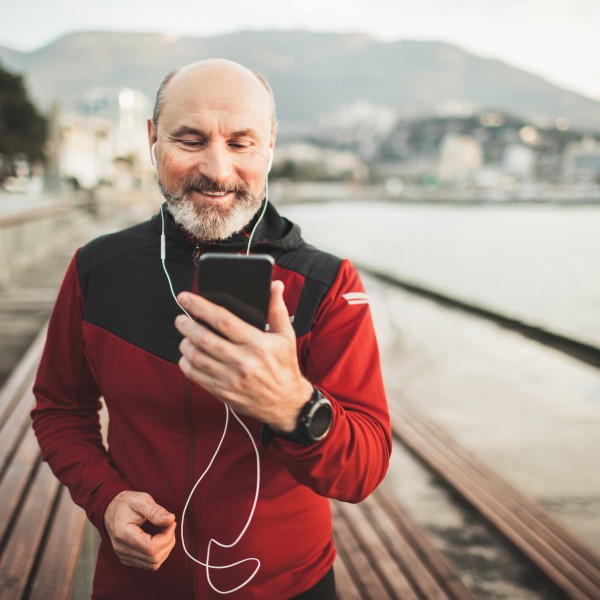 Senior im Sportoutfit schaut auf Smartphone