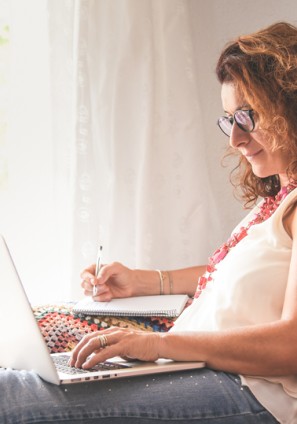 Woman sits at home reading from her laptop and taking notes