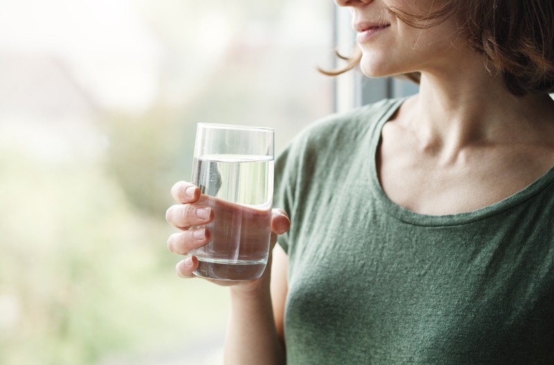 Person standing at window holding glass of water