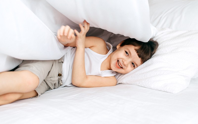 Young child playing and hiding under duvet