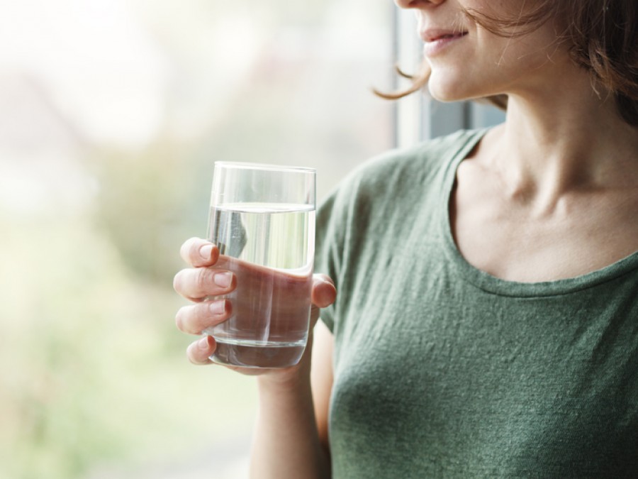 Person standing at window holding glass of water