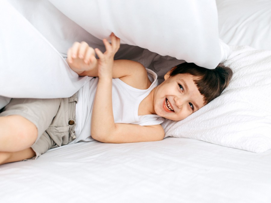 Young child playing and hiding under duvet